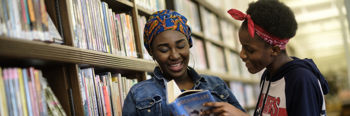 Two teen girls looking at books on library shelves
