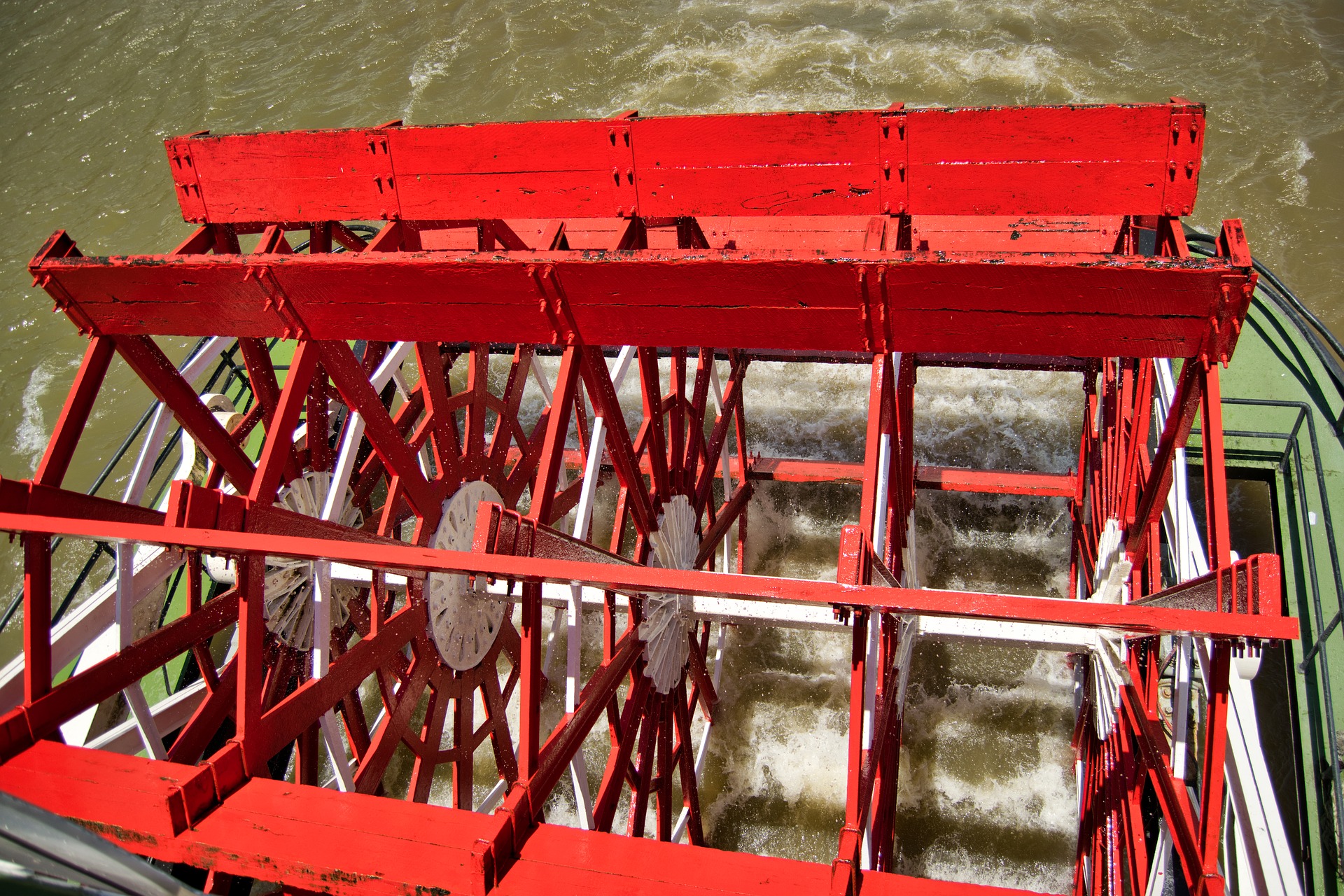 close up of red paddlewheel for a steamboat with river below it