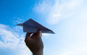 A left hand holding a paper airplane, with a blue sky as the background.