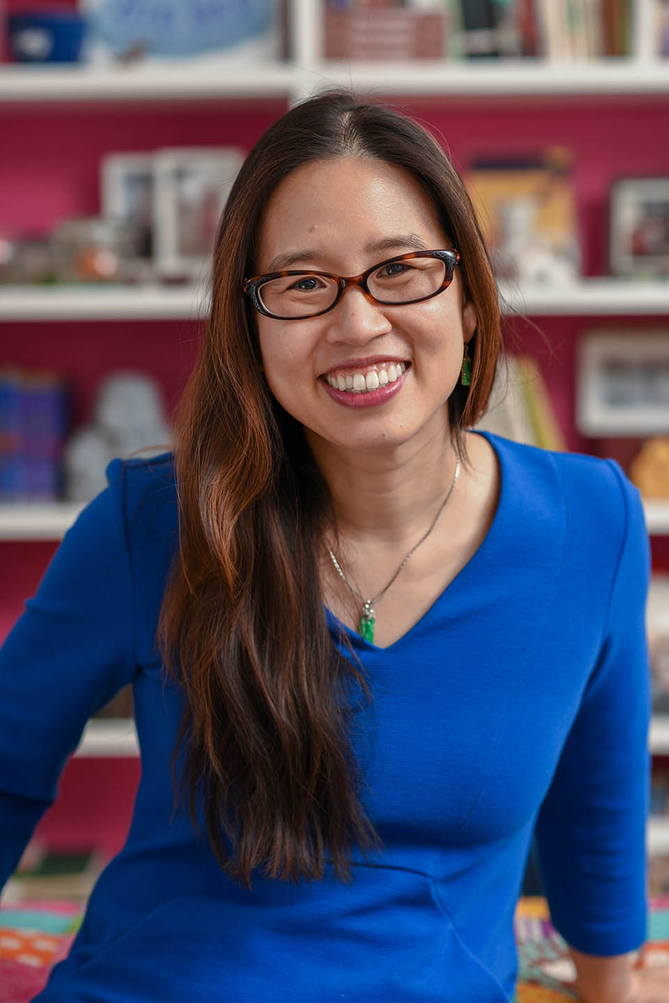 Smiling childrens author Grace Lin in blue sweater with bookshelf behind her