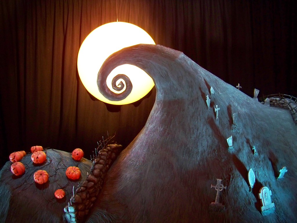 A model of a spiral-shaped hill appears with a light shaped like the moon behind it, with pumpkins and gravestones on the hill.