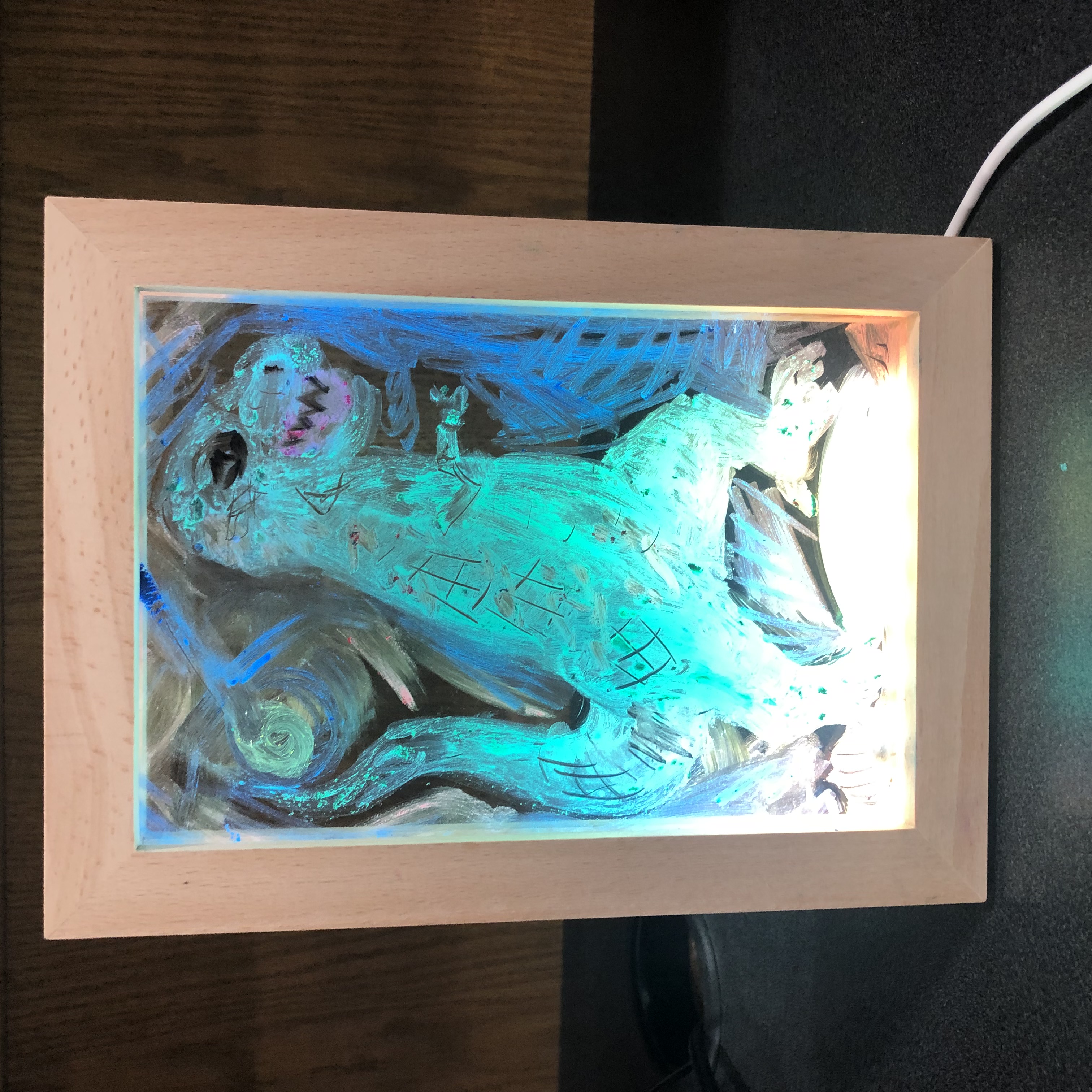 An image of an LED light frame with a drawing of a green T-Rex in the center. There is blue in the background and yellow towards the bottom of the frame, where the light is brightest.
