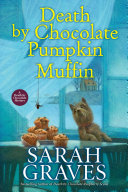 Book cover with yellow and white text reading "Death by Chocolate Pumpkin Muffin" by Sarah Graves, featuring a stack of muffins atop a table, a small dog, and a spider hanging above them