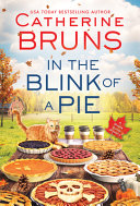 Book cover with blue and red text reading "In the Blink of a Pie" by Catherine Bruns, featuring an outdoor table laden with pies, to-go coffee cups, and an orange cat