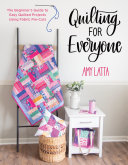 Book cover reading "Quilting for Everyone" by Amy Latta, featuring a colorful quilt hanging from a wooden rack next to a small white nightstand