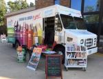 Bookmobile parked on sidewalk with carts of books and colorful signs