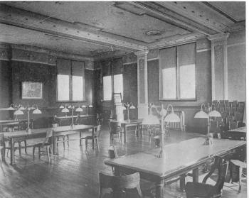 Black and white photo of library interior with reading tables and lamps c. 1903