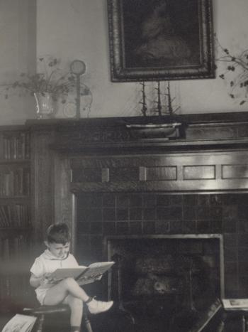 Black and white photo of child reading in front of fireplace in children's library