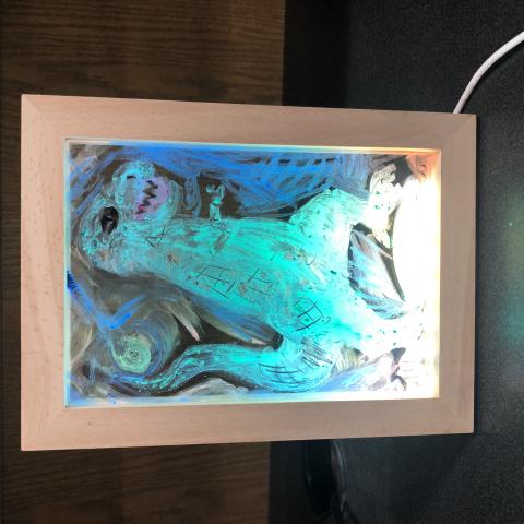 An image of an LED light frame with a drawing of a green T-Rex in the center. There is blue in the background and yellow towards the bottom of the frame, where the light is brightest.