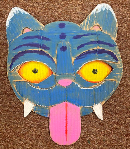 The cardboard head of a cat resembling the feline from the movie "KPop Demon Hunters" appears on a brown carpet background.