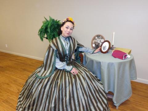 Image of a woman in period attire sitting at a small table