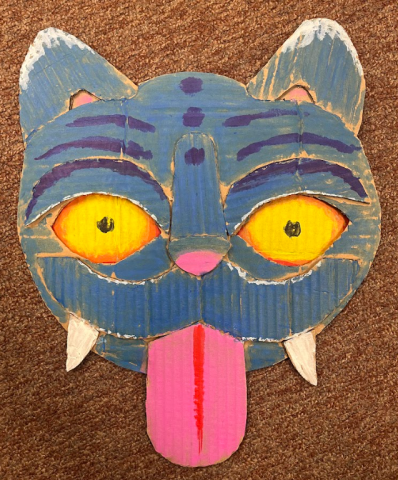 The cardboard head of a cat resembling the feline from the movie "KPop Demon Hunters" appears on a brown carpet background.