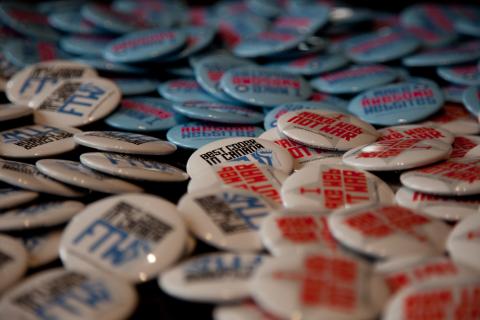 An image of pinback buttons (mainly with red, white, and blue print on each) appear in a pile, filling the frame.