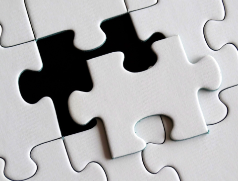 A white puzzle piece has been placed partially atop a black surface, and you can see from the other white pieces surrounding it that it will fit in the gap.