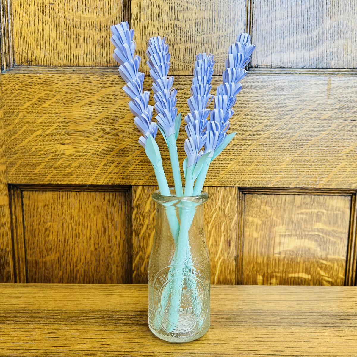 Purple paper flowers in vase with wooden background