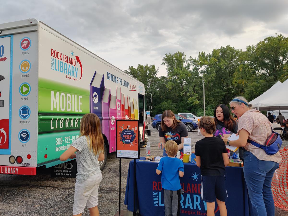 Staff working table at the Greek Fest next to Library2Go bookmobile