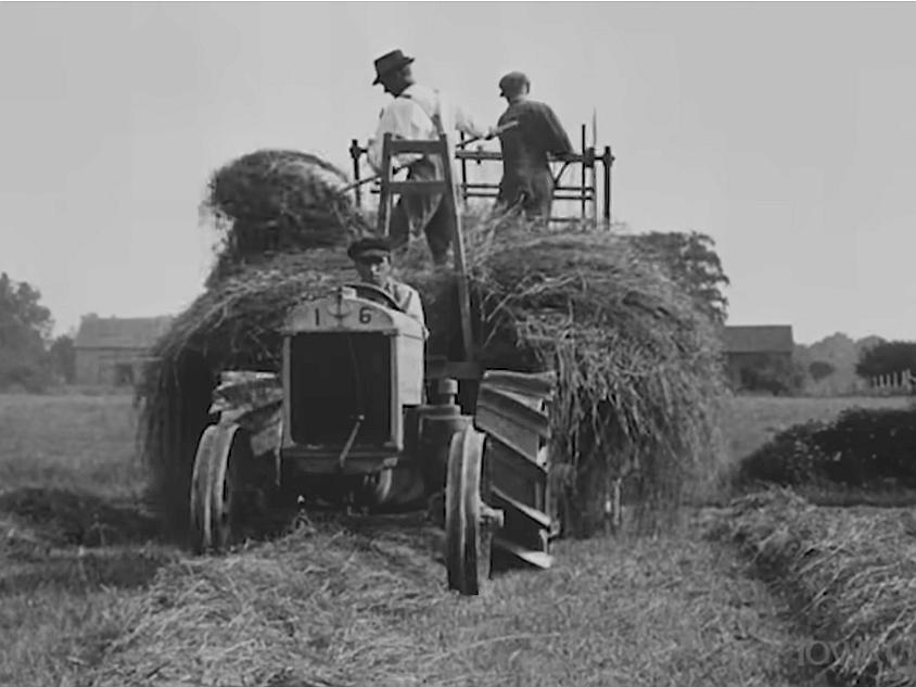 Early tractor with 3 men - a driver and 2 piling straw on the wagon