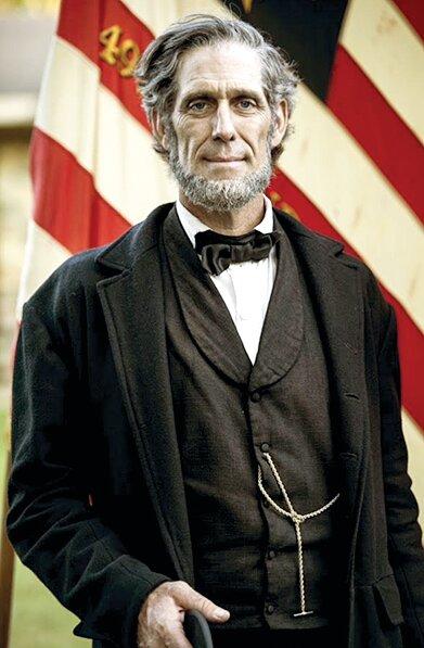 A man resembling Abraham Lincoln posed in front of an American Flag.