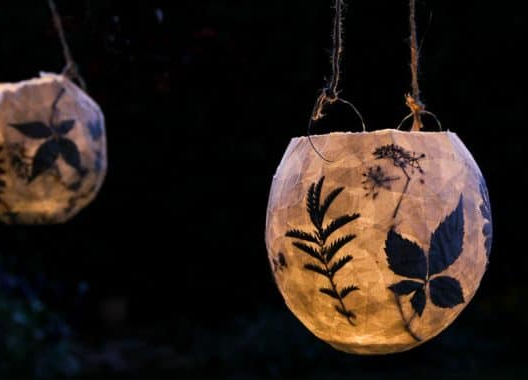 Two paper lanterns made with pressed flowers appear glowing against a dark background.
