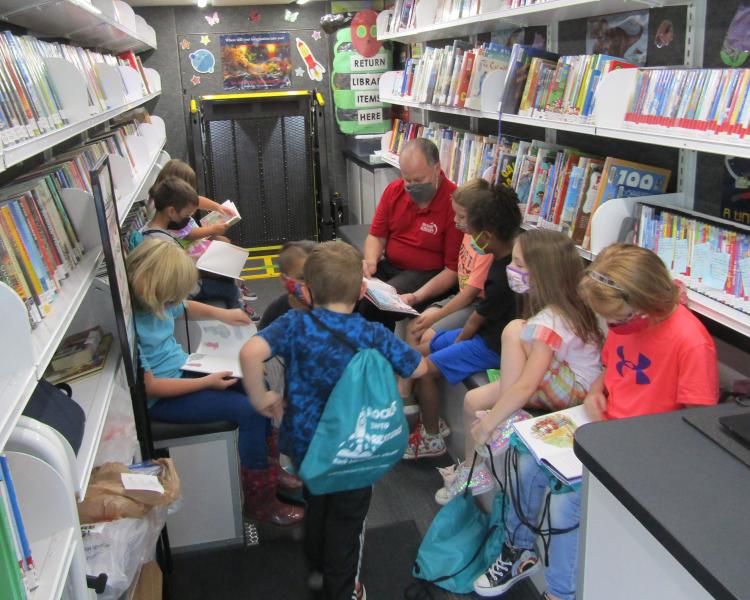 Masked elementary students reading inside the Library2Go bookmobile